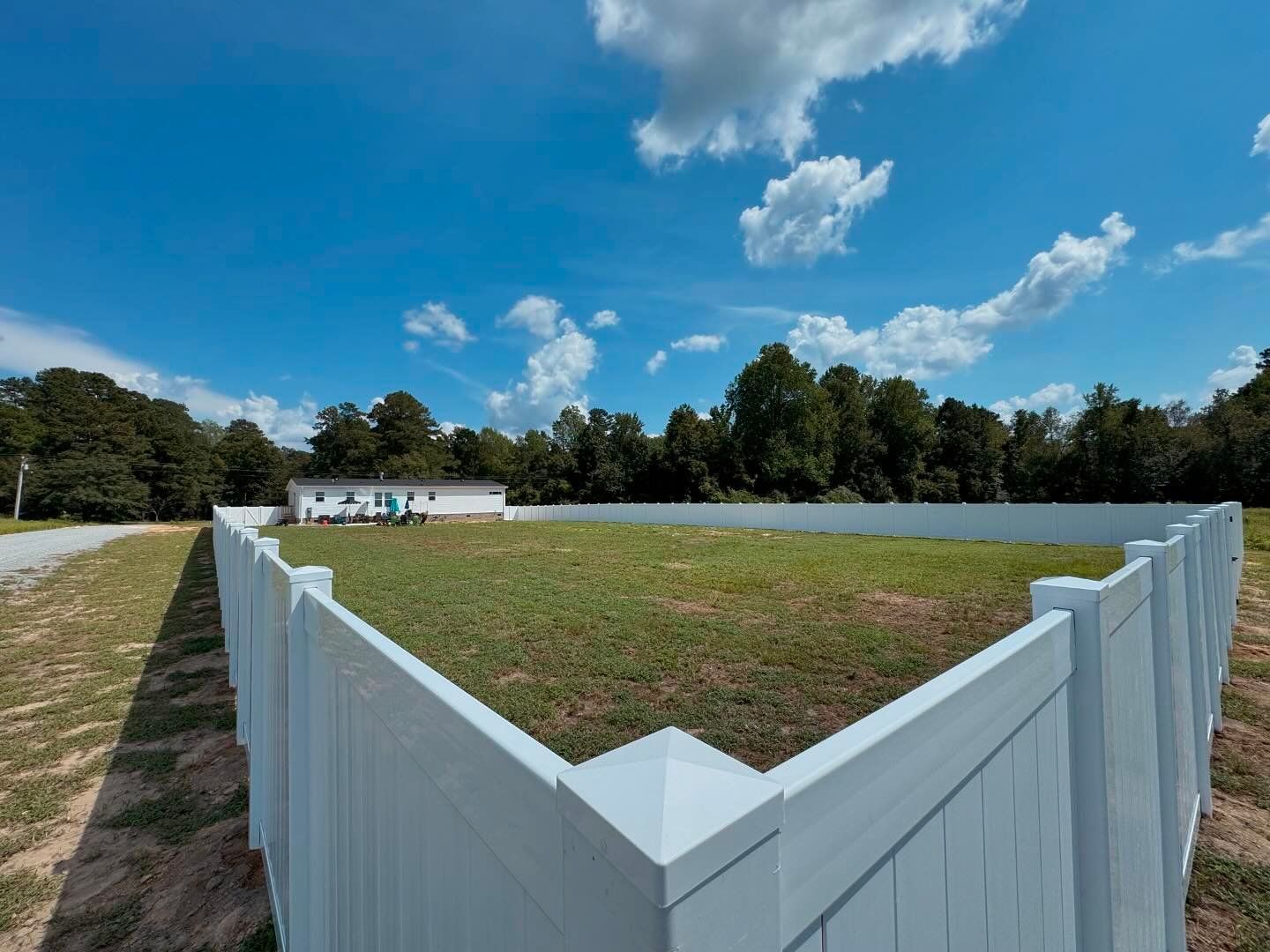 A white fence surrounds a grassy field with trees in the background.