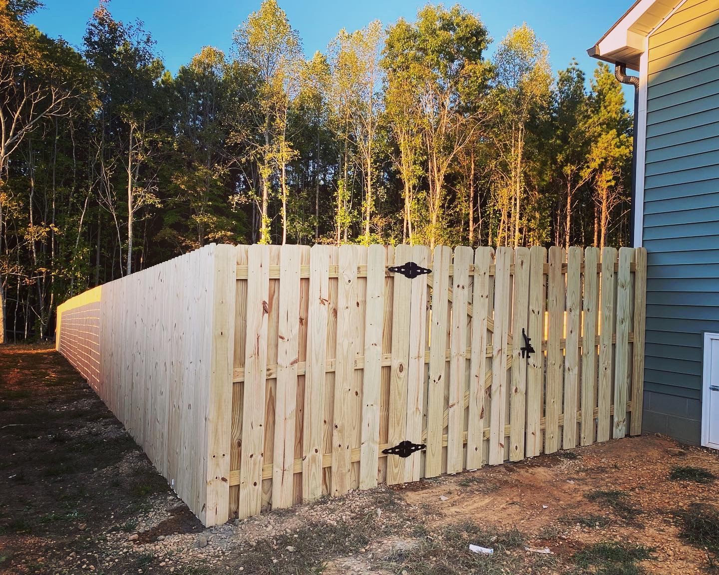A wooden fence is surrounded by trees in front of a house.
