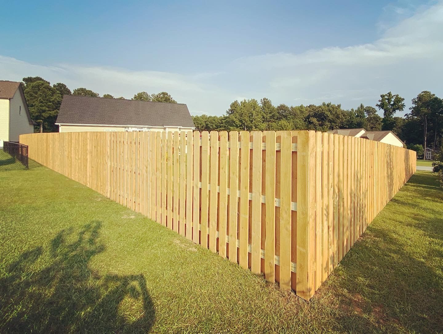 A wooden fence is in the middle of a lush green yard.