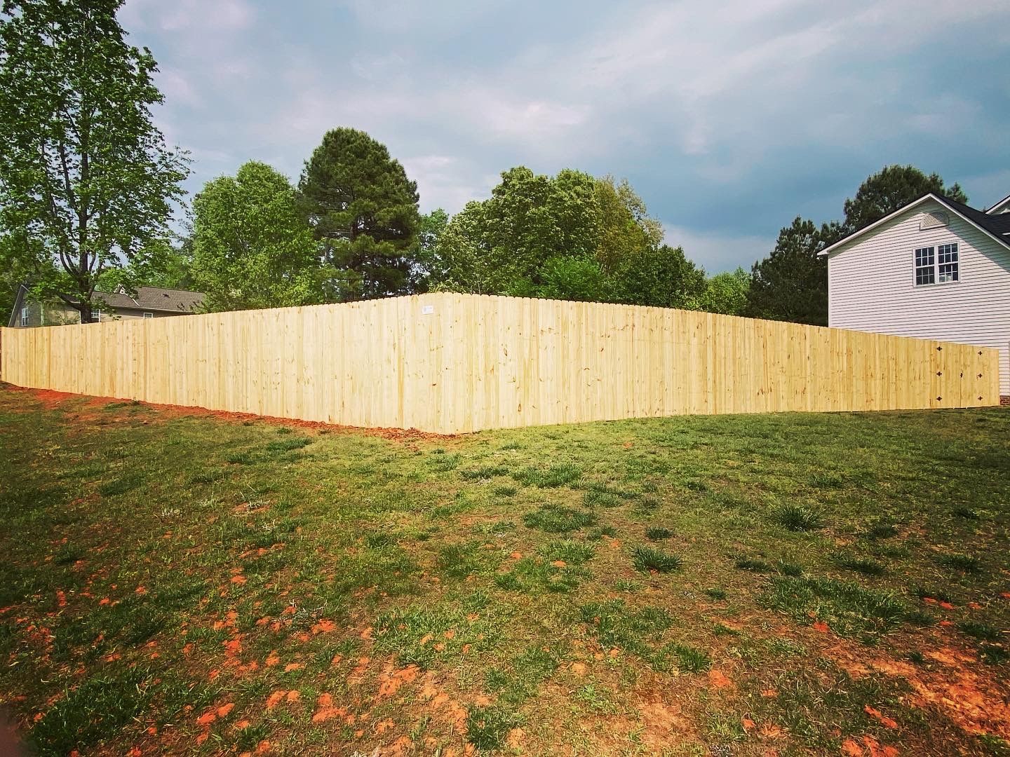A wooden fence surrounds a lush green field in front of a house.