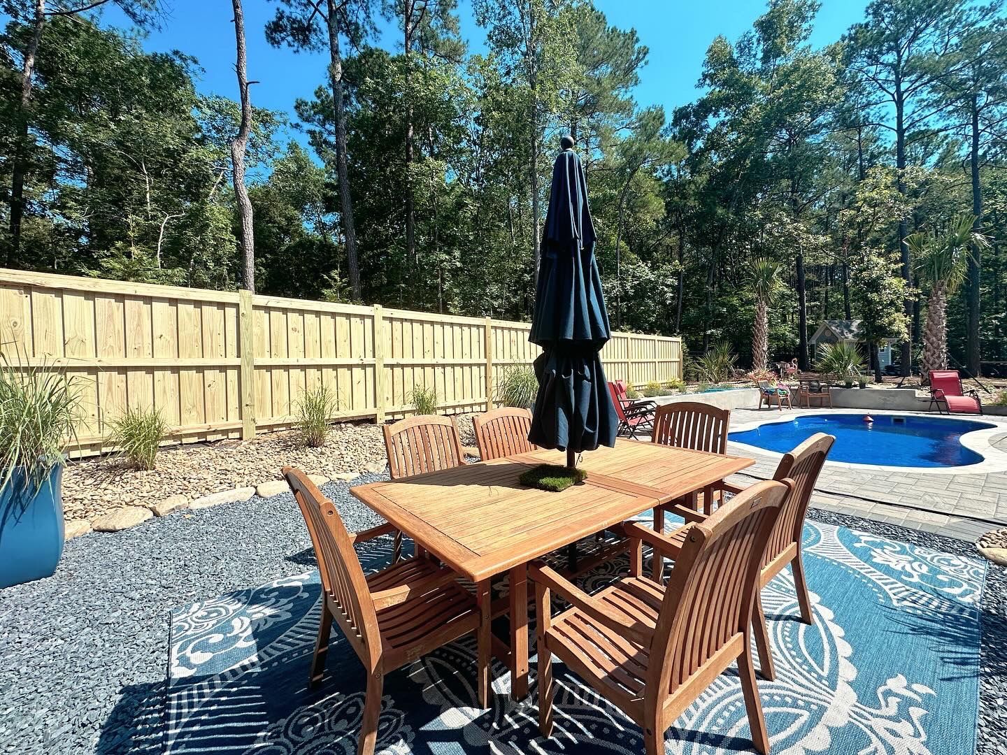 A patio with a table and chairs and an umbrella next to a pool.