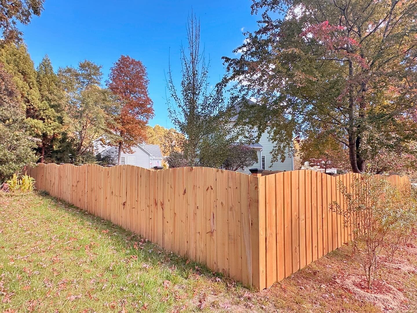 A wooden fence is surrounded by trees and grass in a yard.