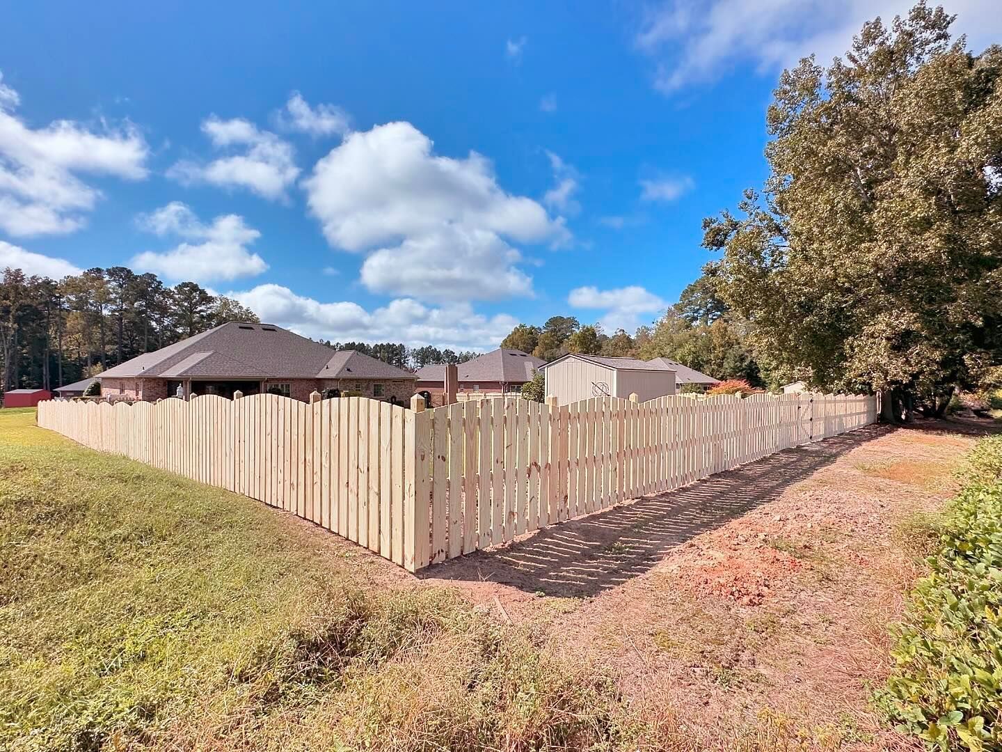 A wooden fence surrounds a house on a sunny day.