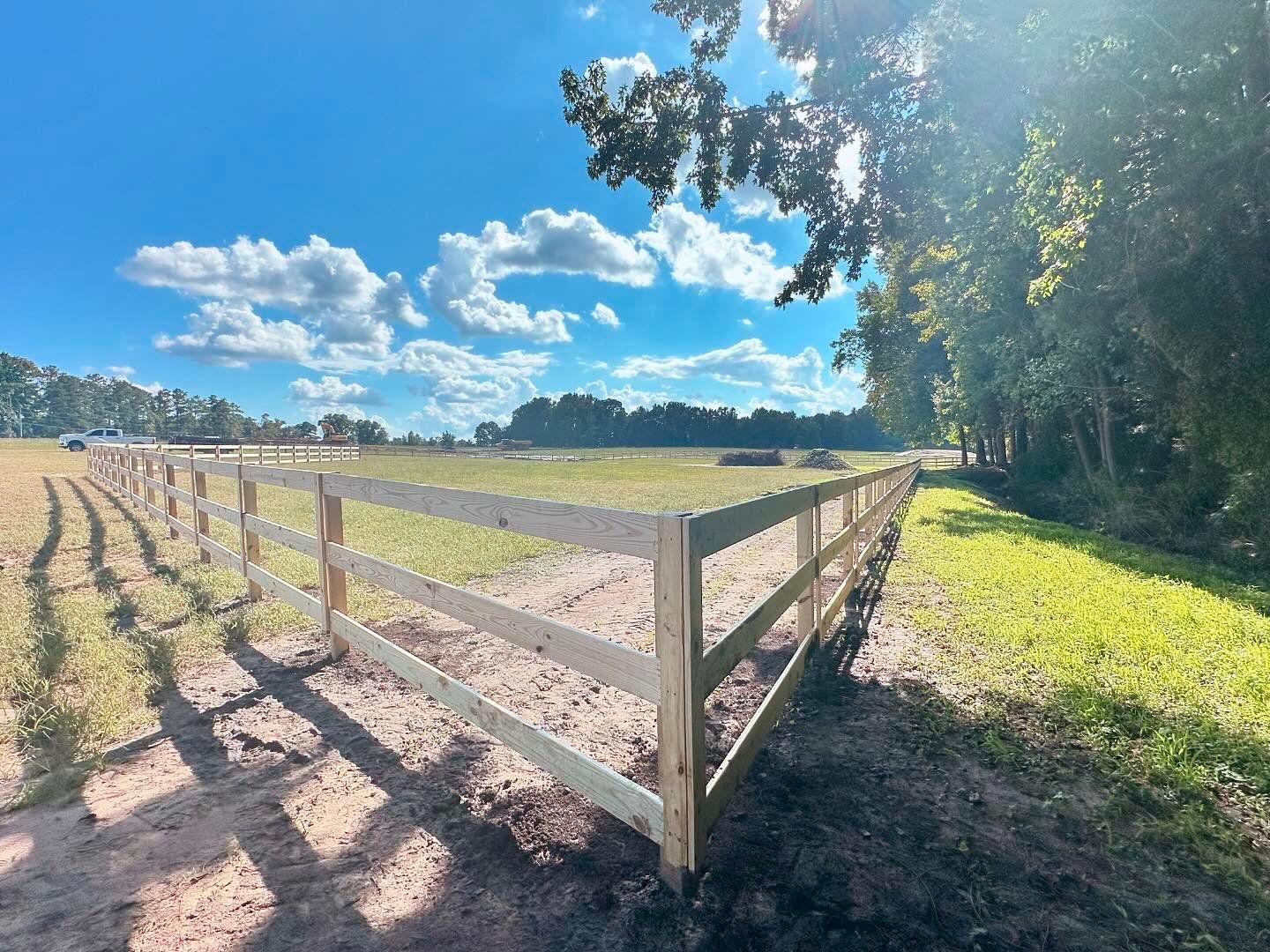 A wooden fence surrounds a grassy field on a sunny day.