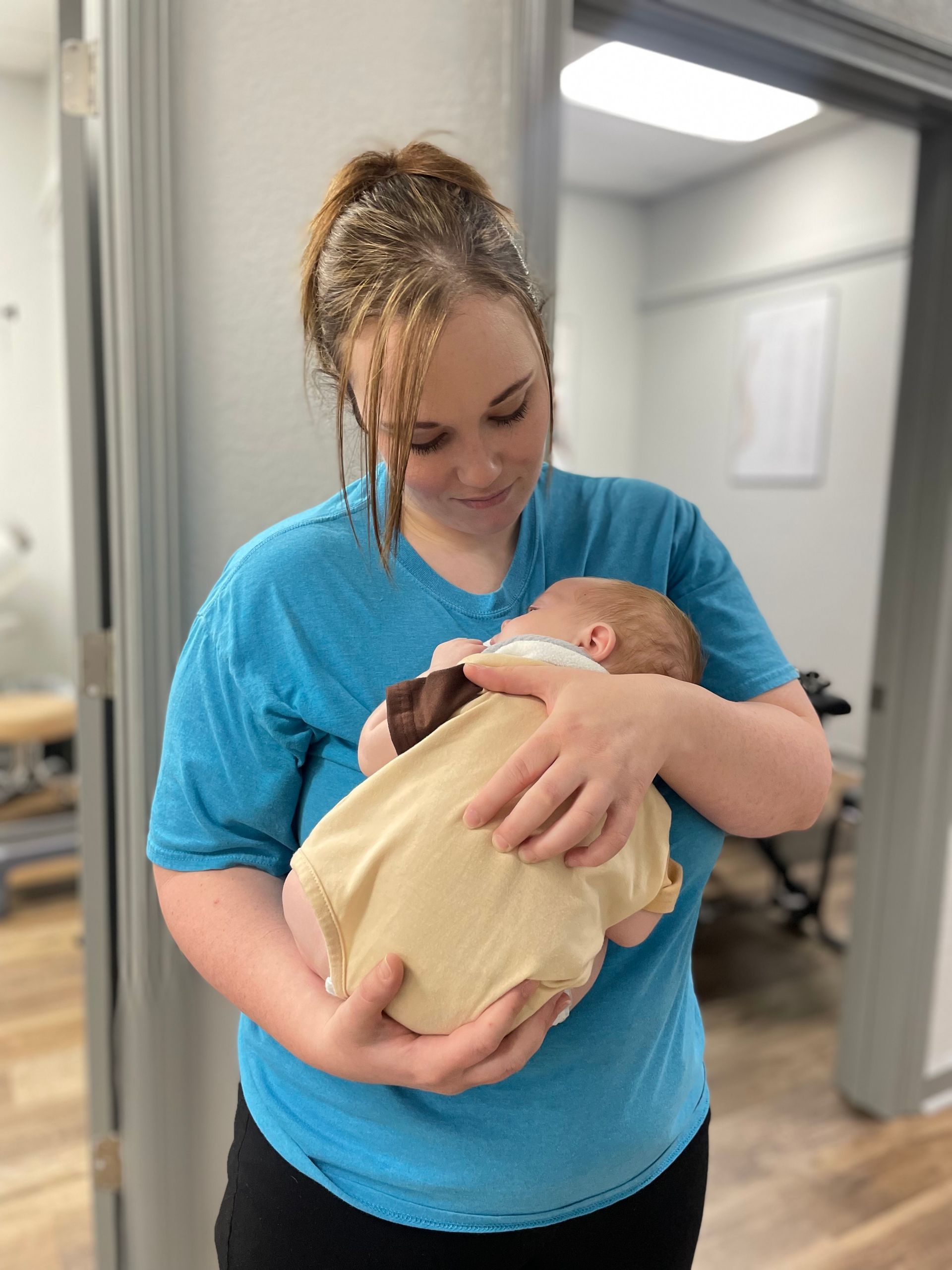 Woman in blue shirt cradling a baby wrapped in a beige blanket in a hallway
