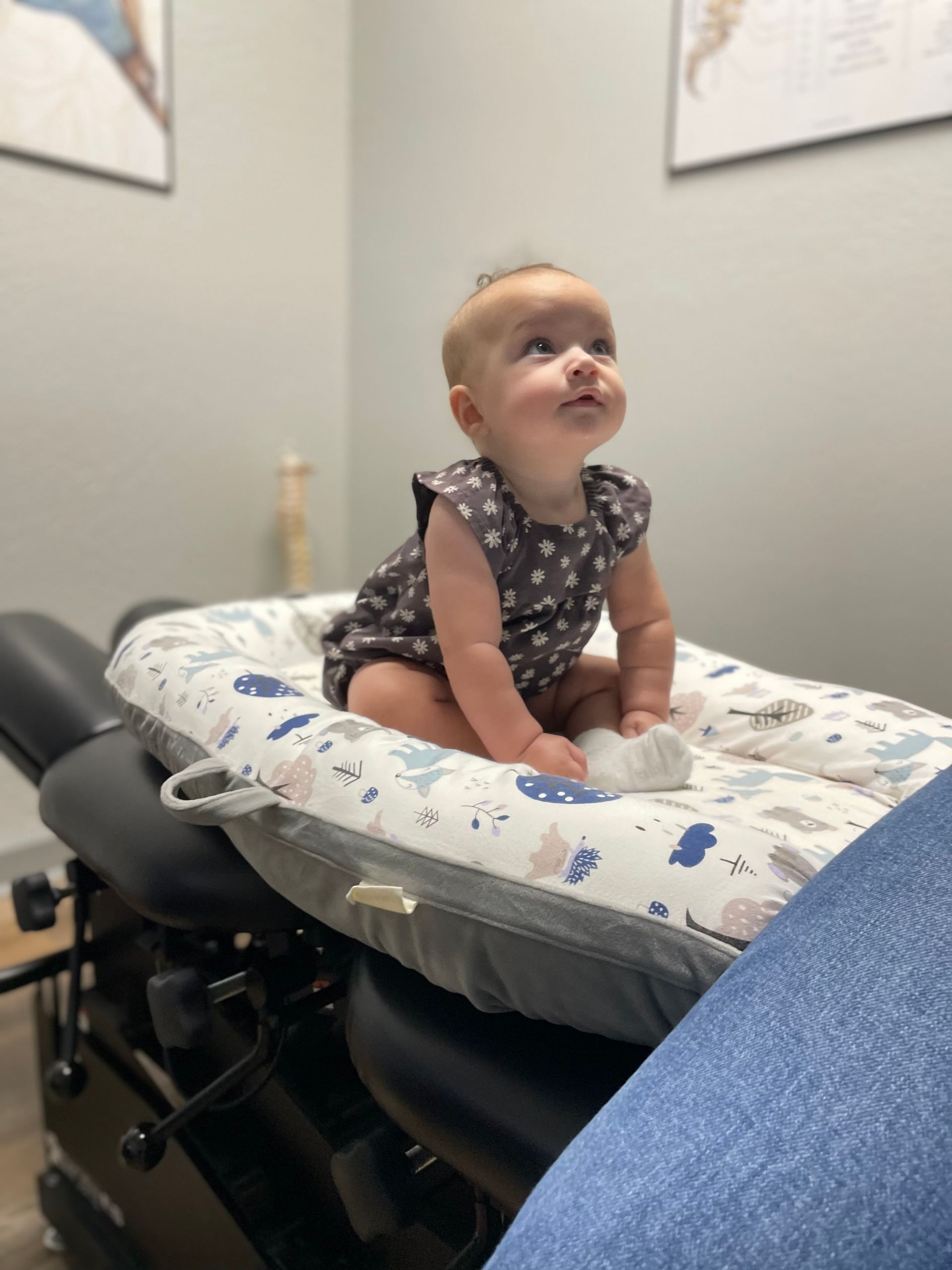 Baby sitting on a chiropractic table, looking upward in a clinic room.