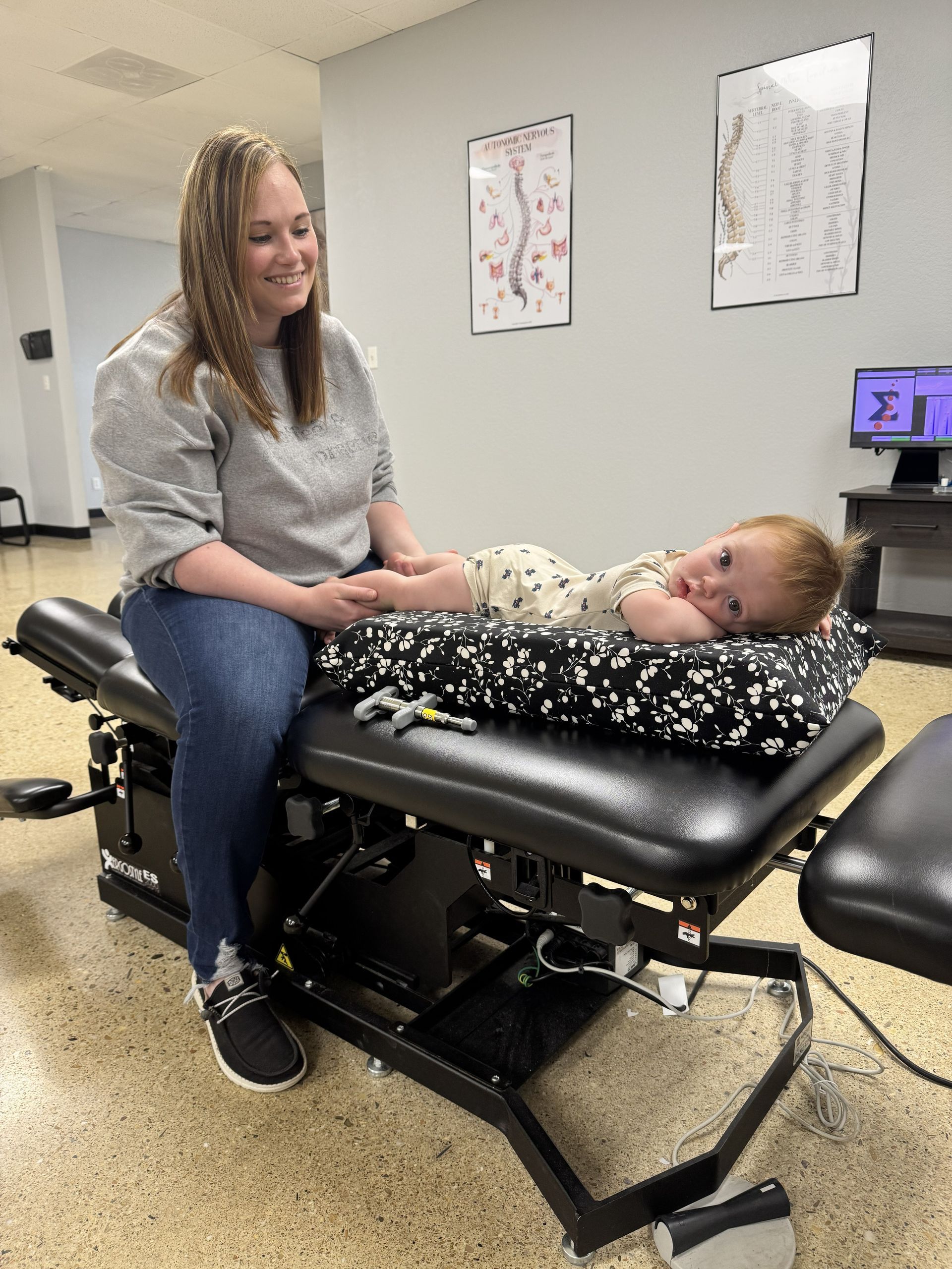 Woman sitting beside a child lying on a padded exam table in a clinic room
