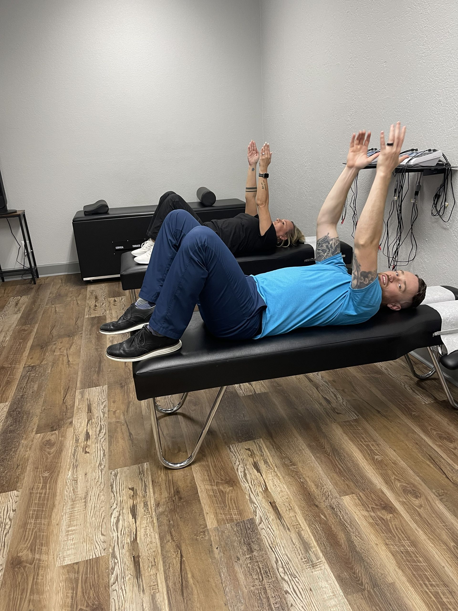 People doing a floor exercise in a gym, lying on mats and raising their arms.