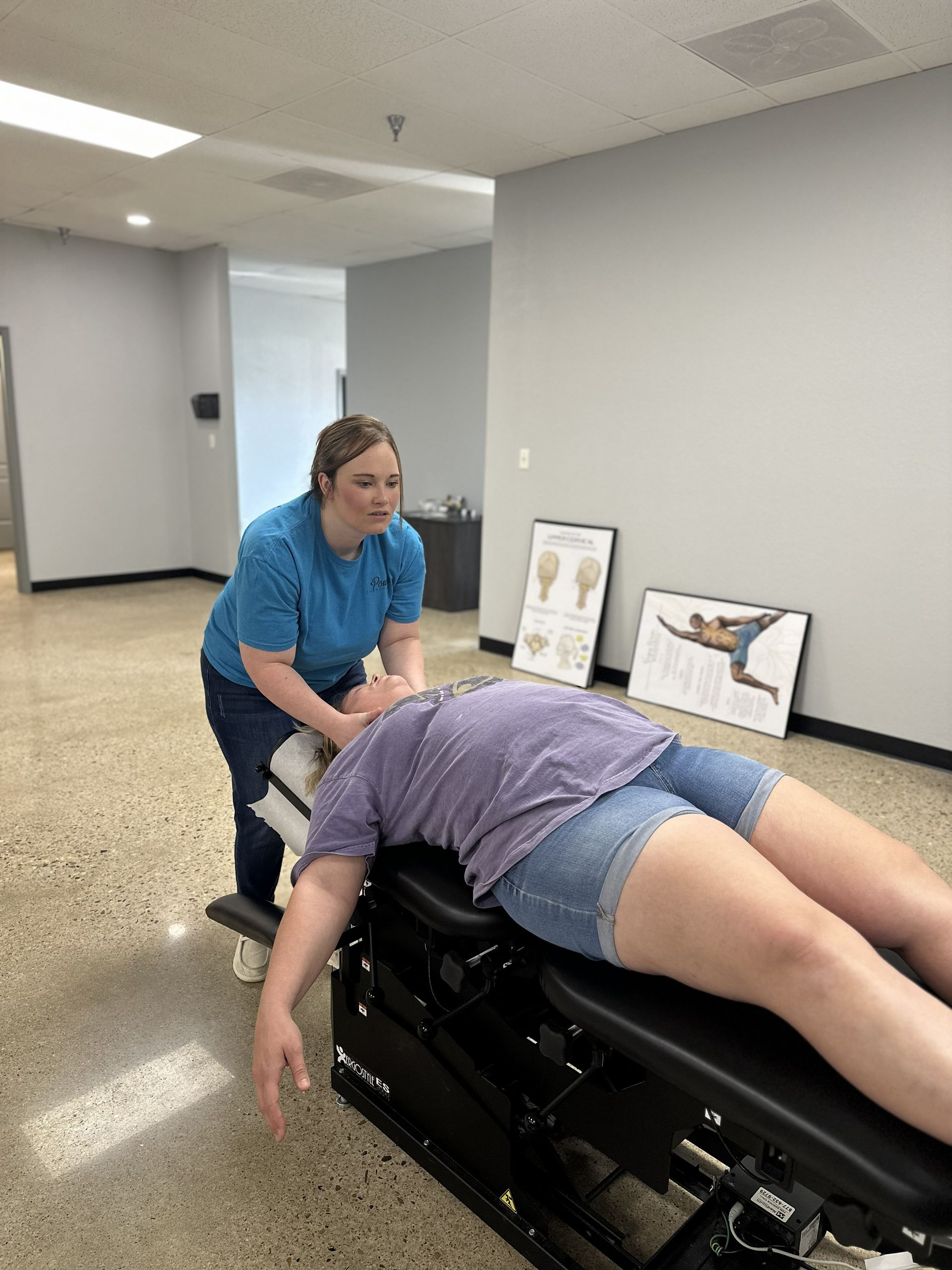 Chiropractor adjusting a patient lying face down on a treatment table in a clinic room.