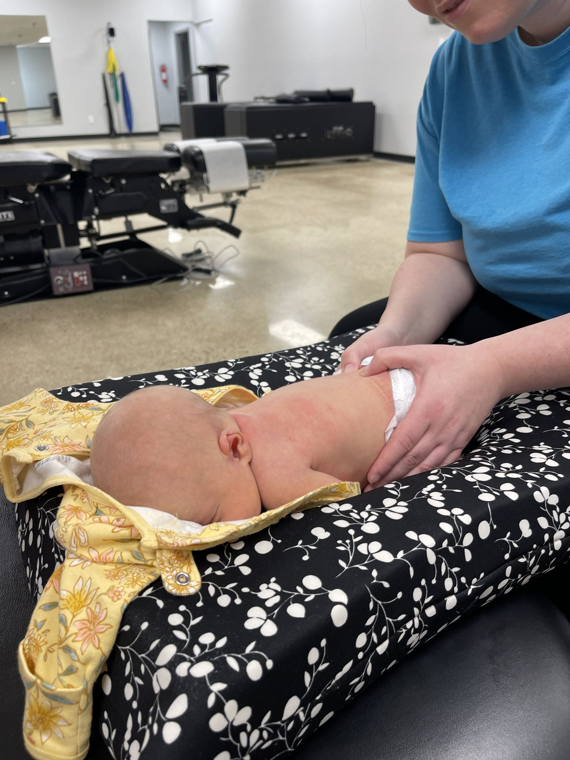 Person holding a newborn on a patterned cushion in a clinical room