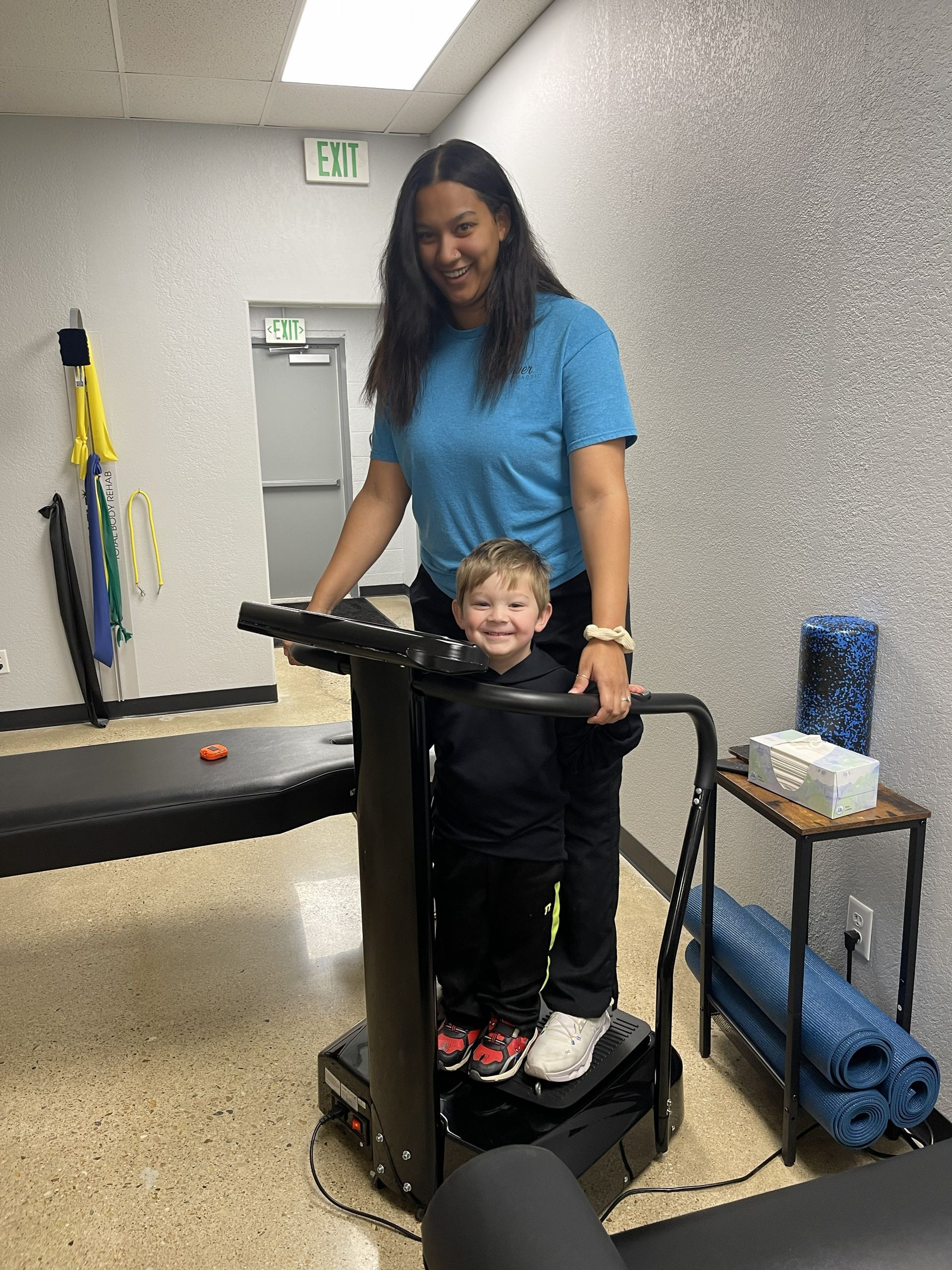Adult and child standing on a treadmill in a gym, with exercise equipment in the background.
