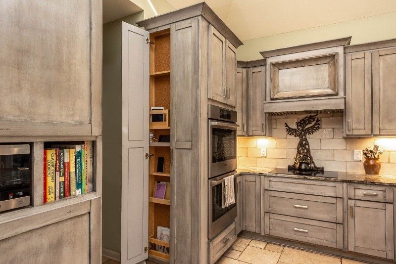 A kitchen with gray cabinets , stainless steel appliances , and a pull out pantry.