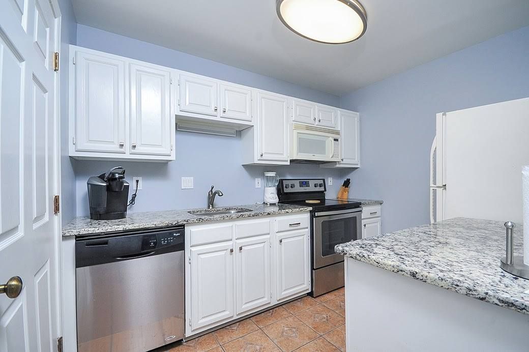 A kitchen with white cabinets , stainless steel appliances and granite counter tops.
