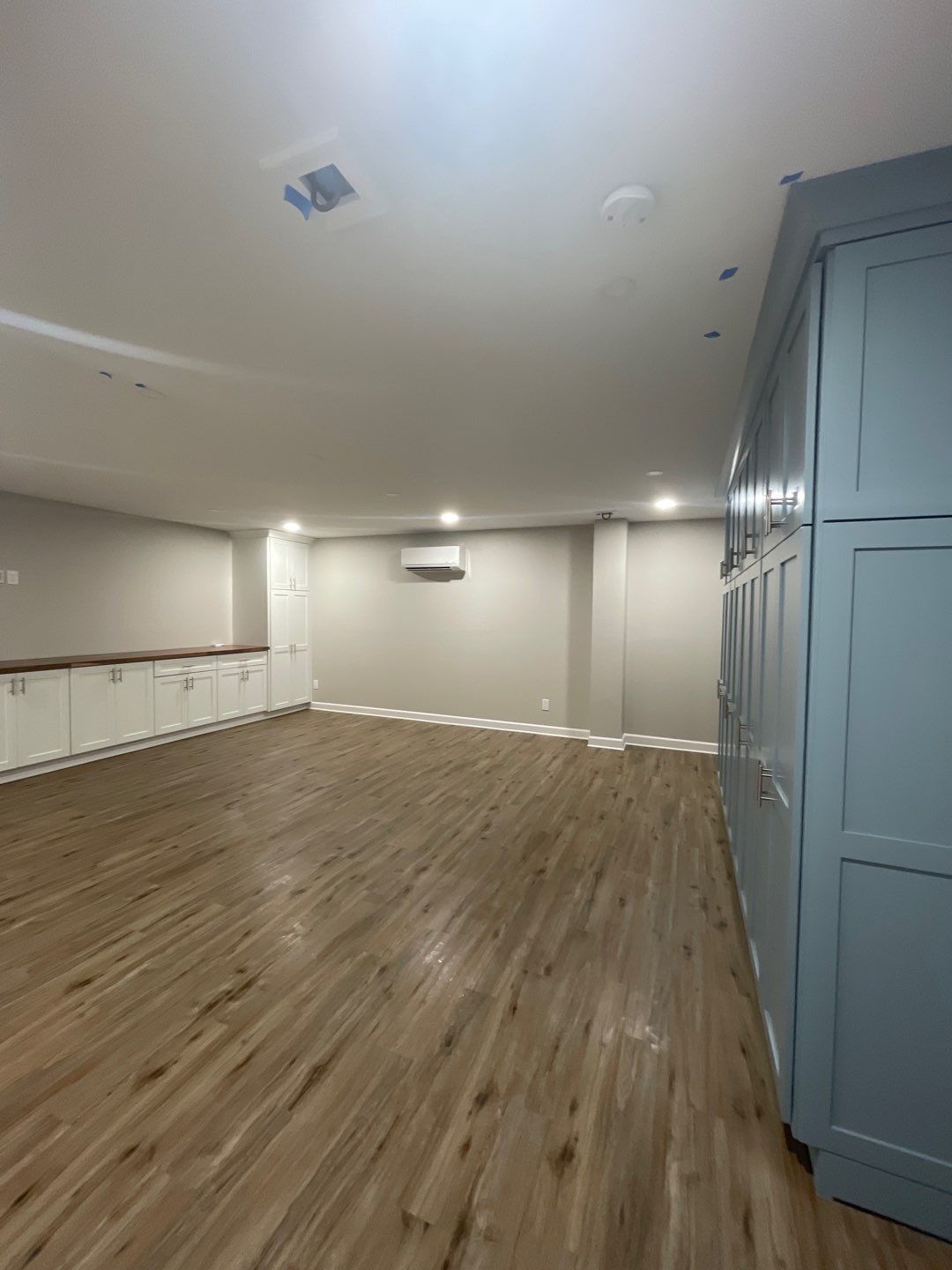 An empty basement room with hardwood floors and blue cabinets