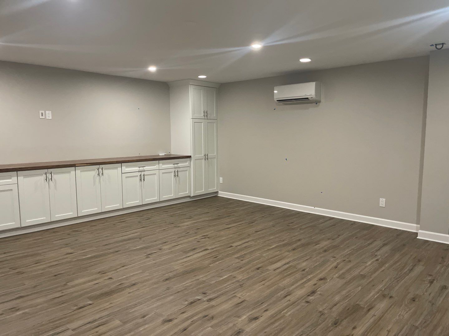 A large empty basement room with hardwood floors and white cabinets