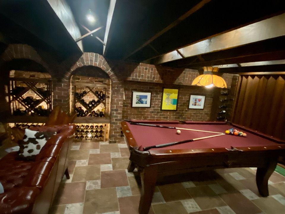 Basement recreation room with pool table, brick accents, wine racks, and leather sofa.