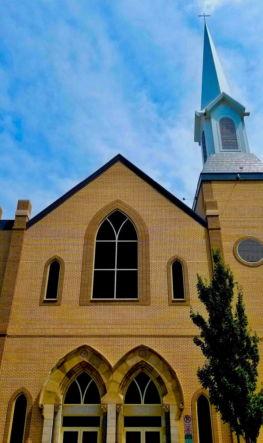 Tan brick church with tall steeple and cross against a blue sky.