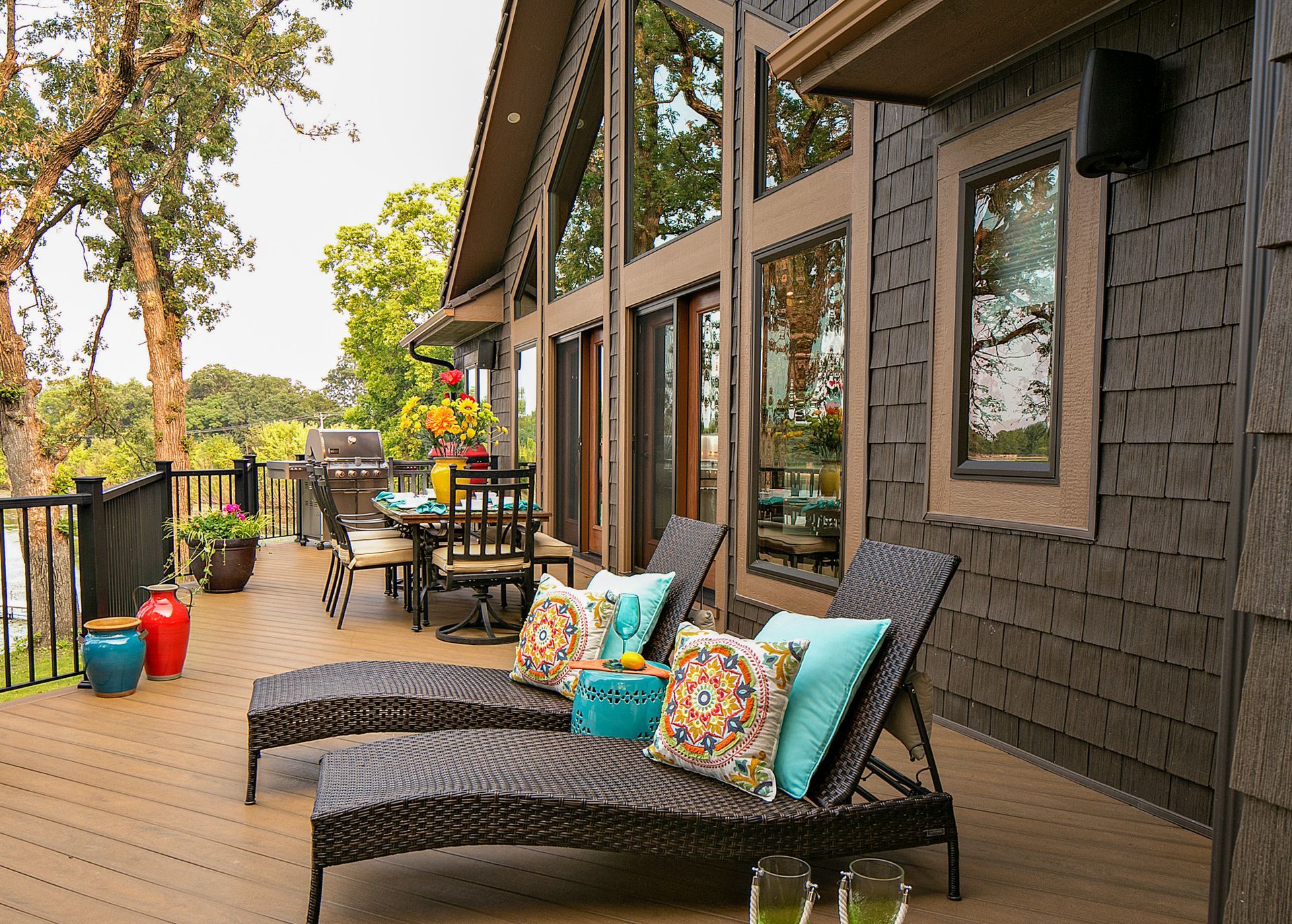 Deck with lounge chairs, dining table, and dark brown siding, overlooking a scenic view.