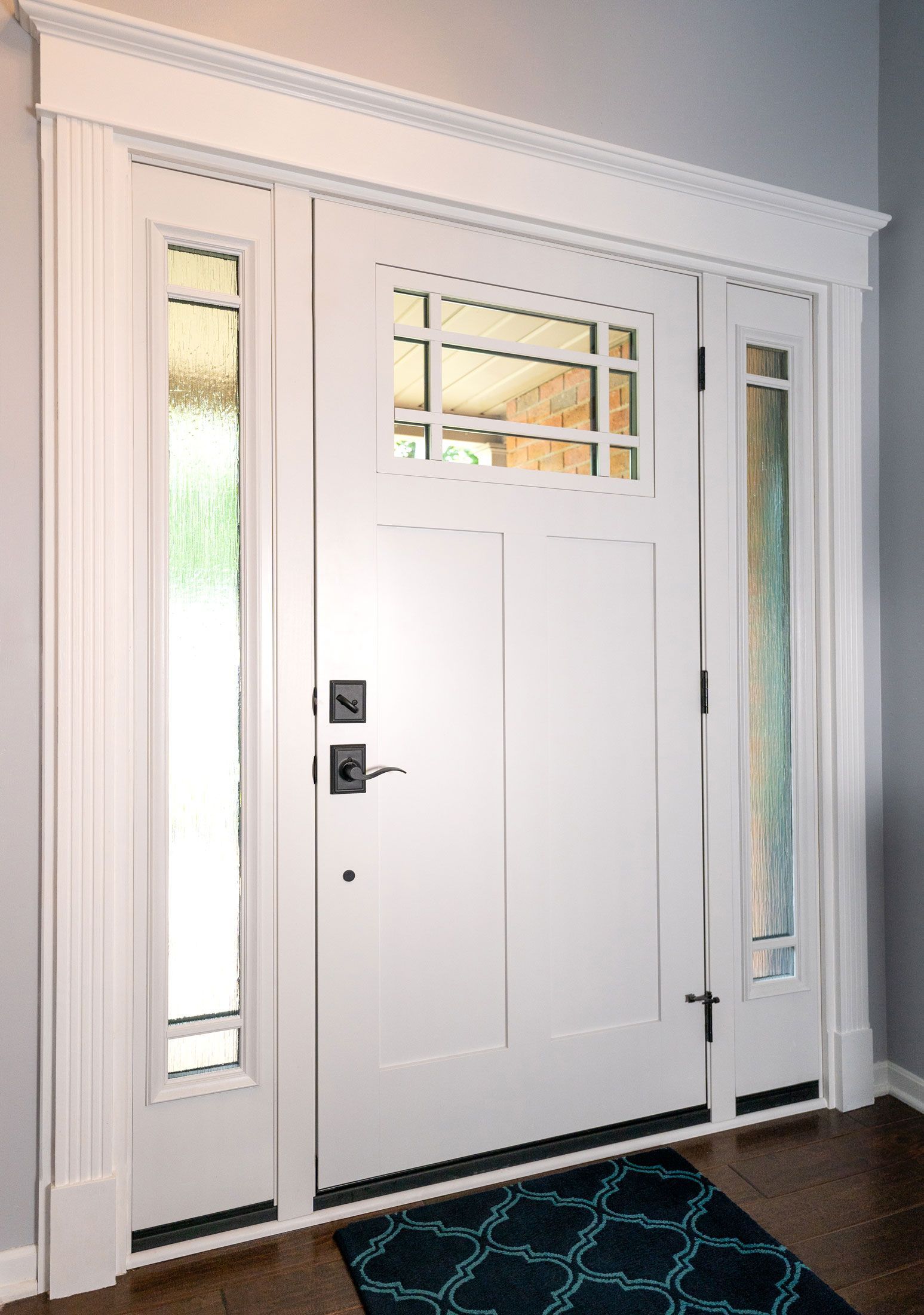 White front door with sidelights, featuring glass panels, and a decorative trim above.