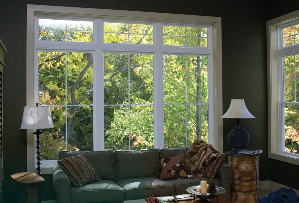 A living room with a large window overlooking trees, a couch, lamps, and a small table.