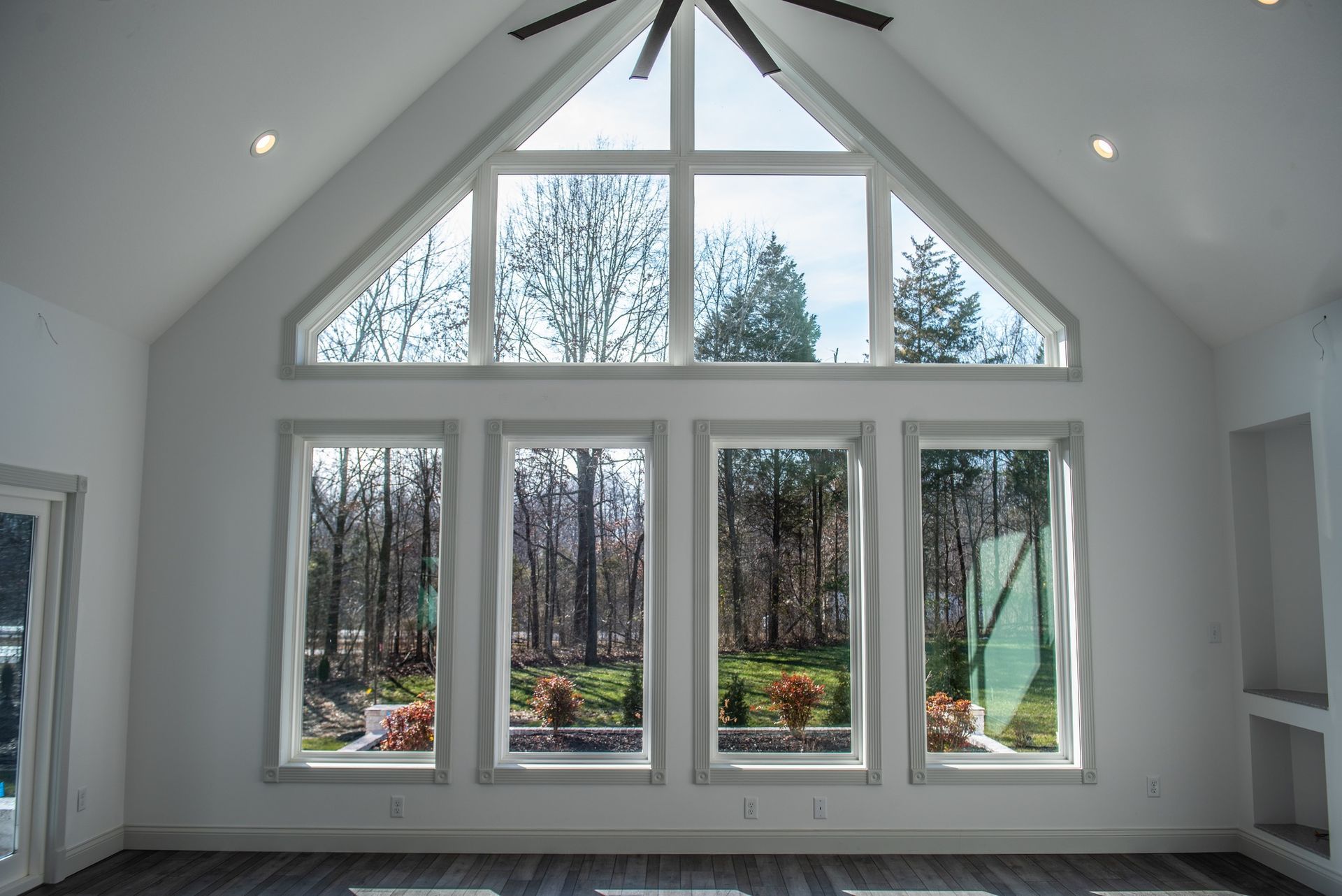Interior view of a room with large windows overlooking trees. White walls, grey trim, and dark flooring.