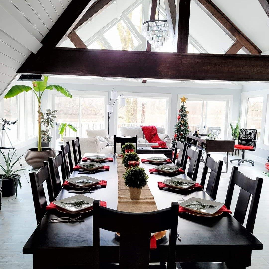 Formal dining room set for Christmas with long dark table, place settings, and small decorated tree.