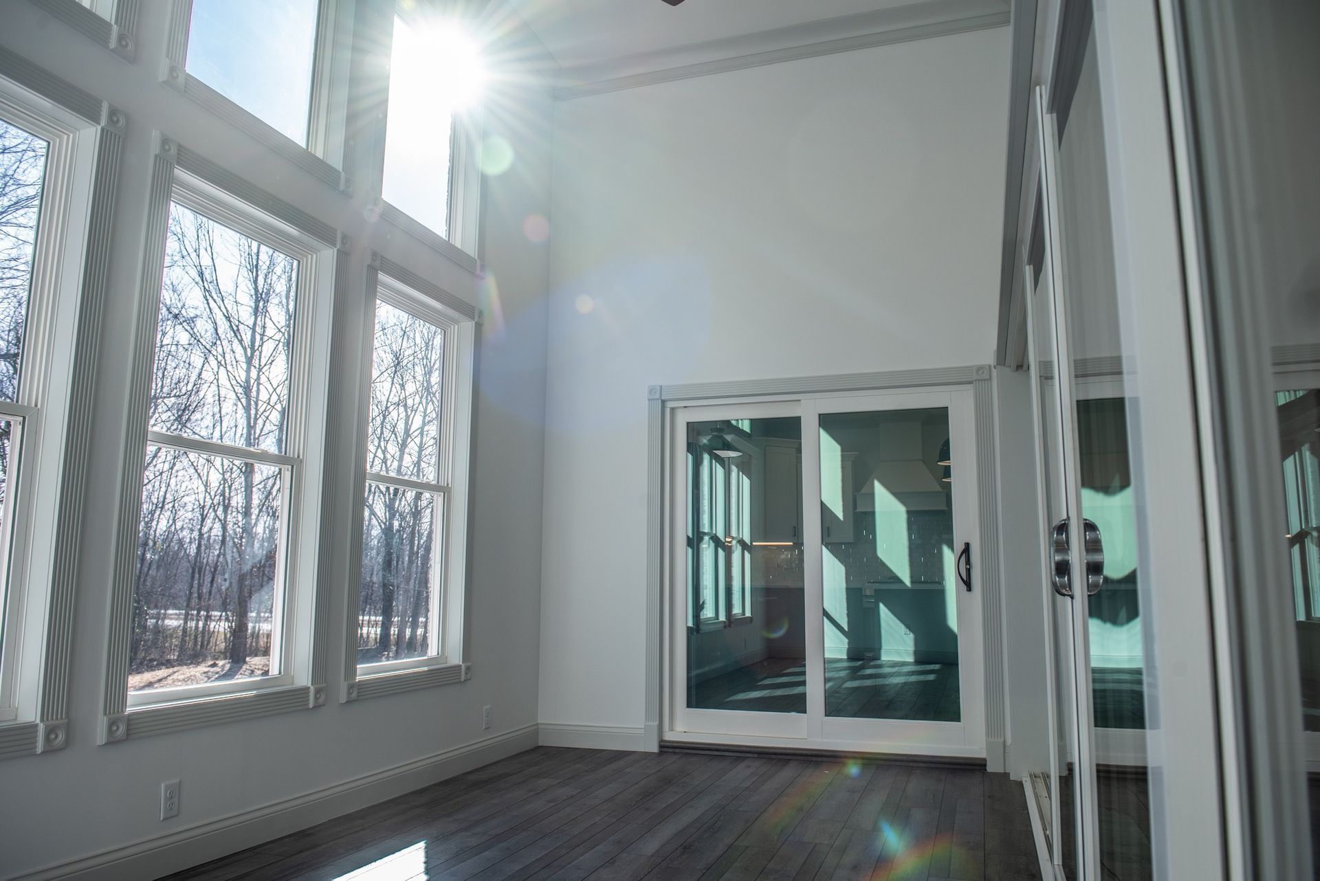 Sunlit room with large windows, sliding glass door, and dark wood floor.