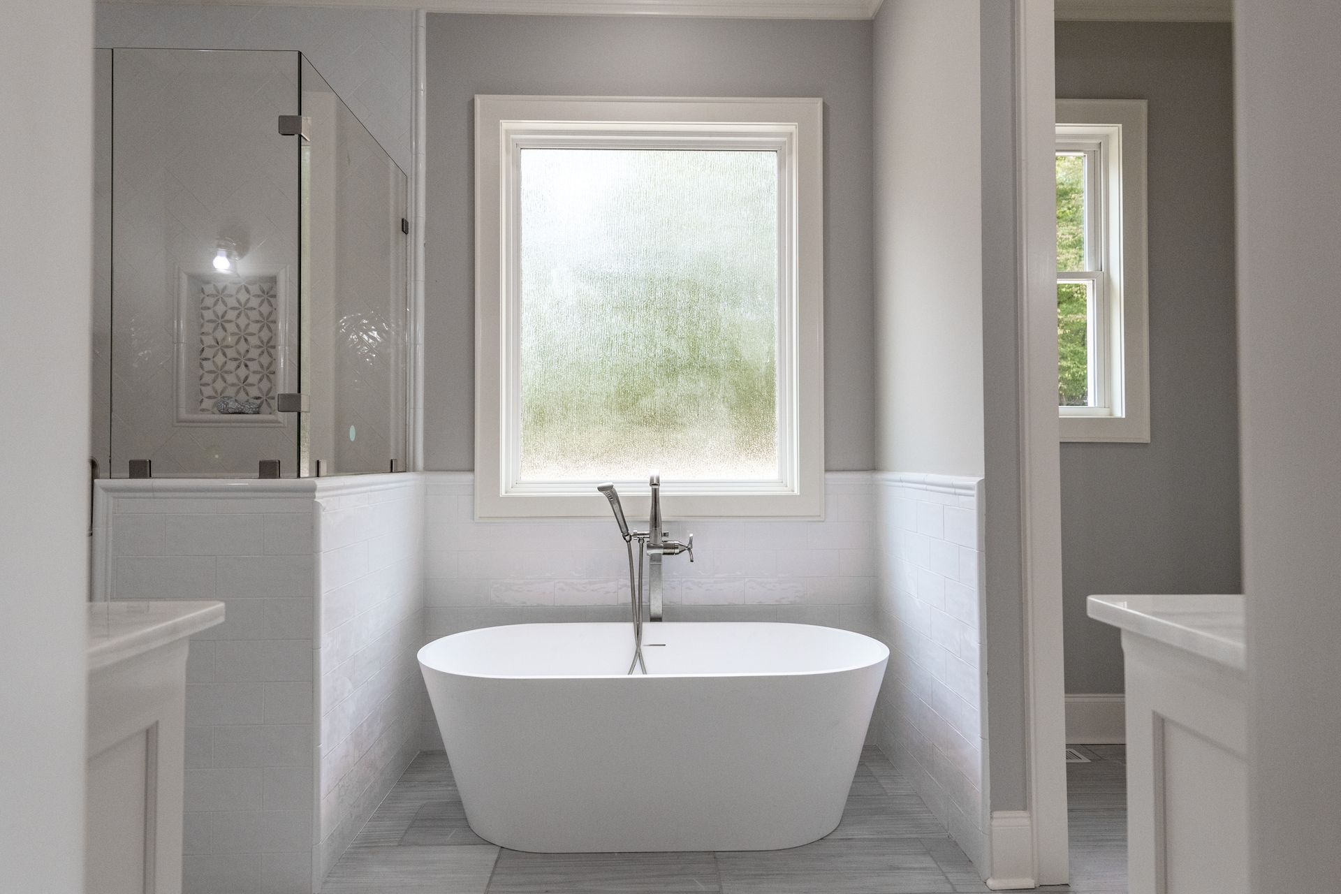 Modern bathroom with a white bathtub, frosted window, and glass shower enclosure.