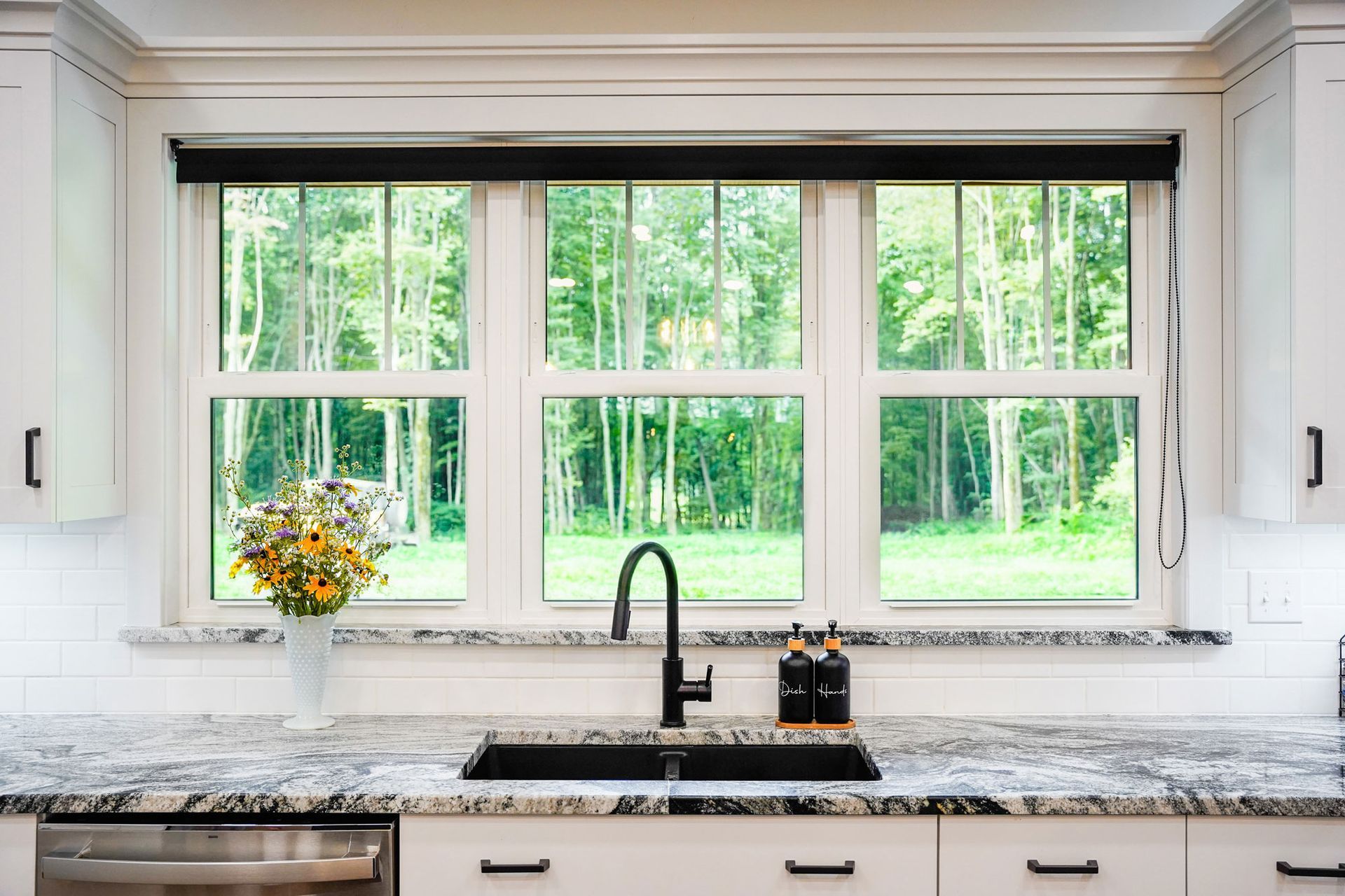 Kitchen sink with granite countertop and window overlooking trees. Black faucet and cabinet handles.