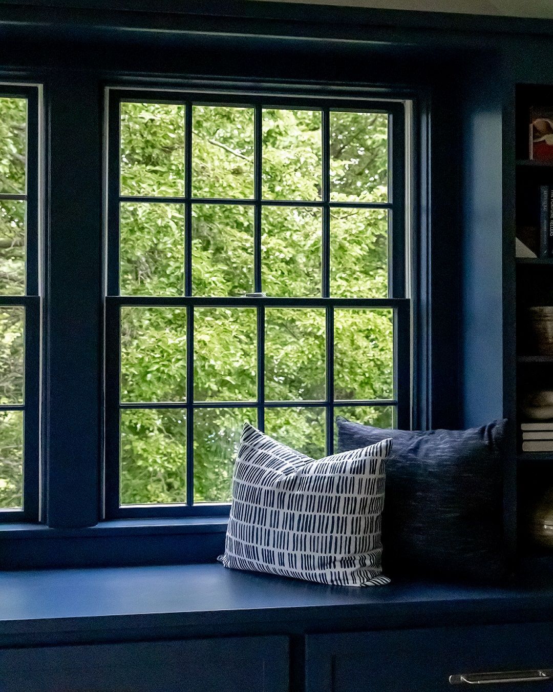 Blue window seat with two decorative pillows, looking out onto trees.