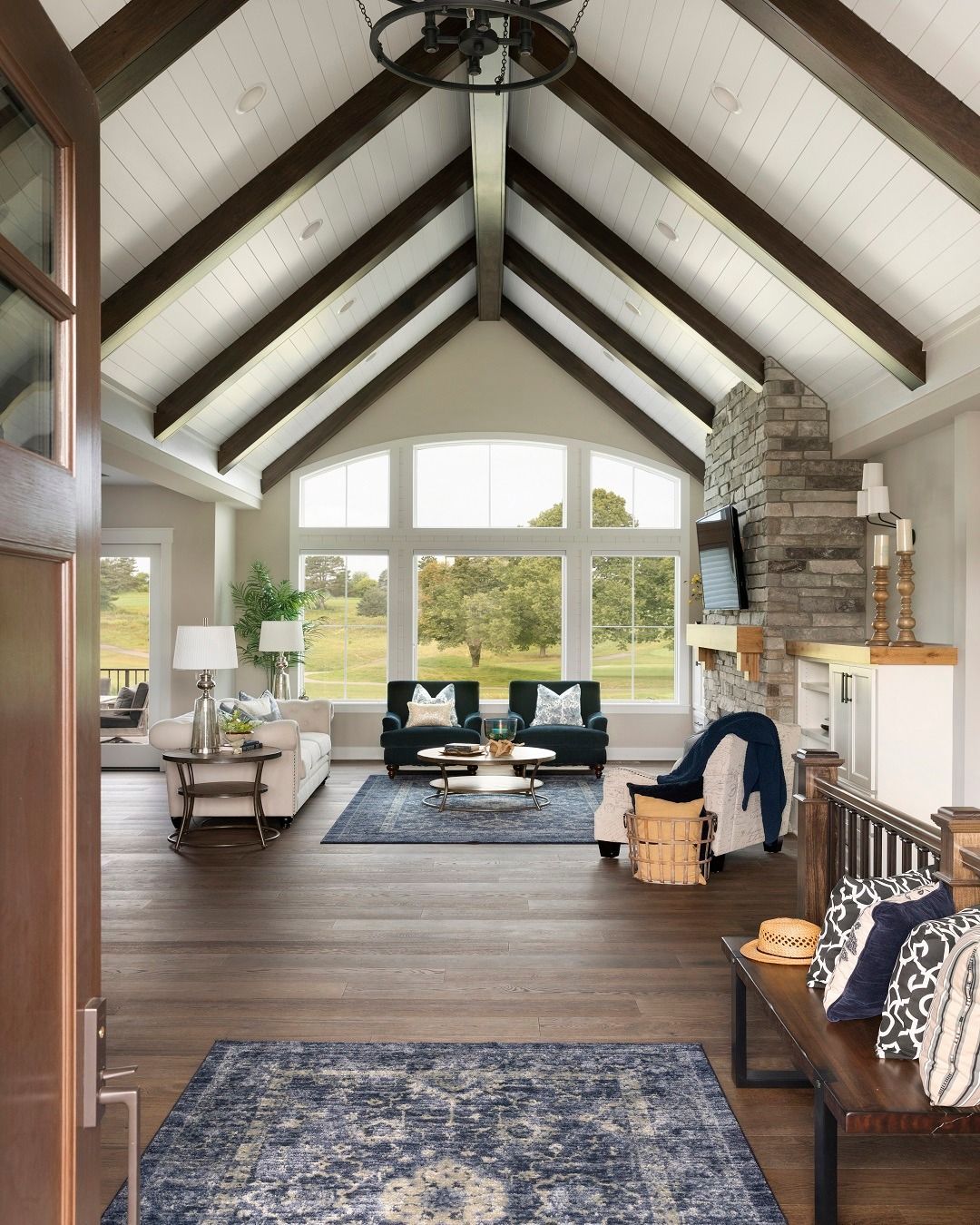 Interior of a home with a high ceiling, wood beams, and large windows overlooking a green landscape.