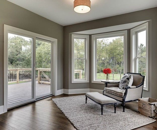 Room with bay window and sliding glass door, neutral walls, chair and ottoman on a rug.