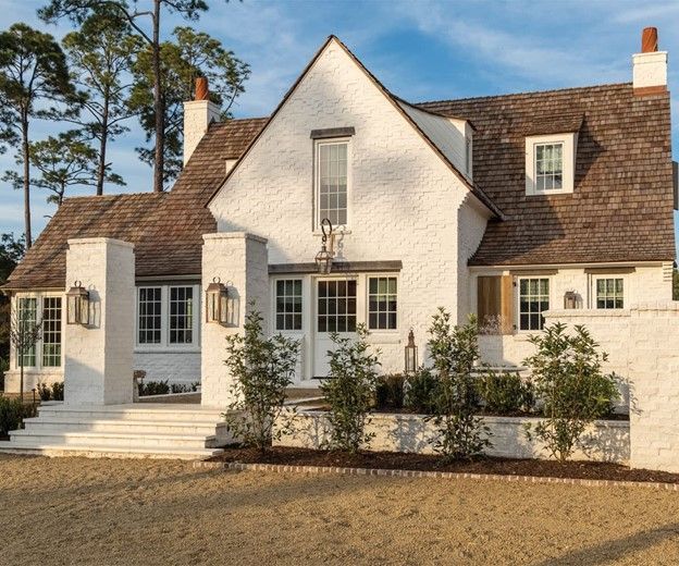 White stucco house with brown roof and brick accents, steps leading to entrance, trees.