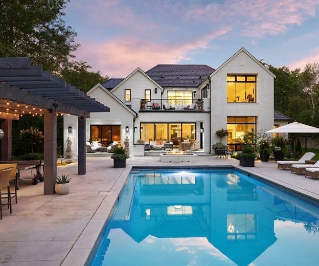 White house with a pool and patio at sunset. The pool reflects the sky and the house lights.