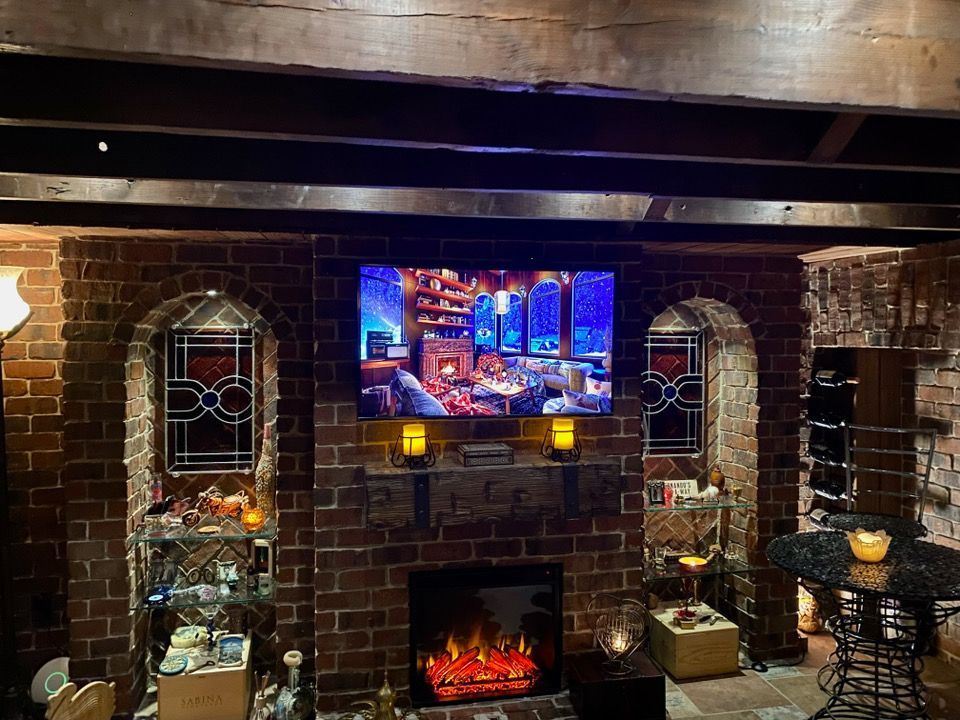Cozy brick-walled room with fireplace and TV; two arched stained-glass windows flank the screen.