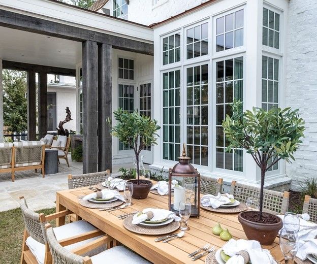 Outdoor dining table set for a meal, with chairs, plants, and a house in the background.