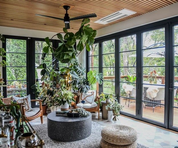 Living room with plants, black framed glass doors, wooden ceiling, and a deck view.