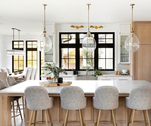 Modern kitchen with island, pendant lights, black-framed windows, and light wood cabinetry.