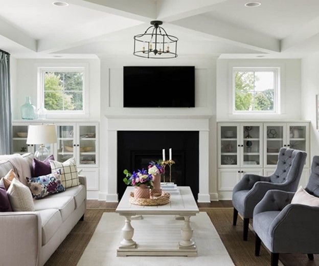 Living room with fireplace, white walls, light gray furniture, and a black chandelier.