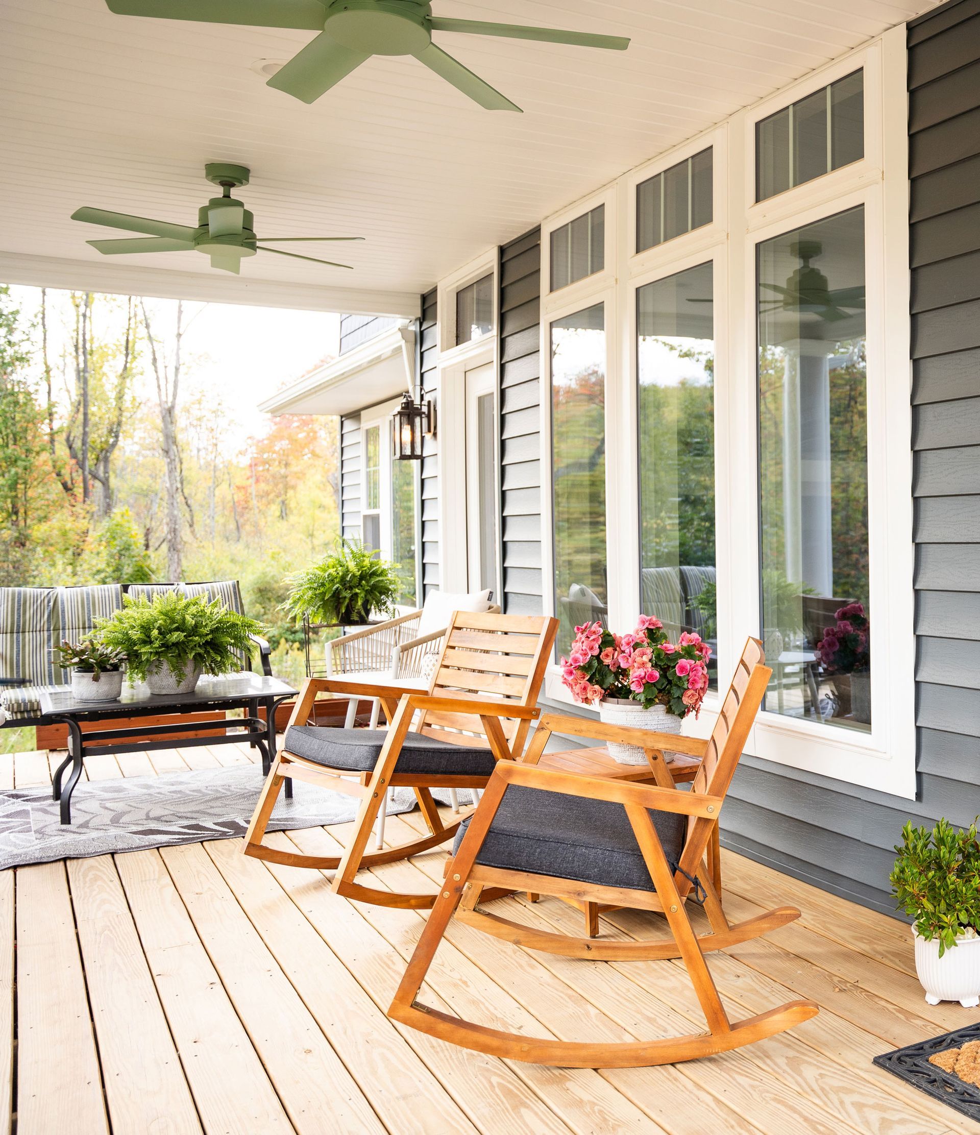 Wooden rocking chairs on a covered porch with green ceiling fans, overlooking a garden.