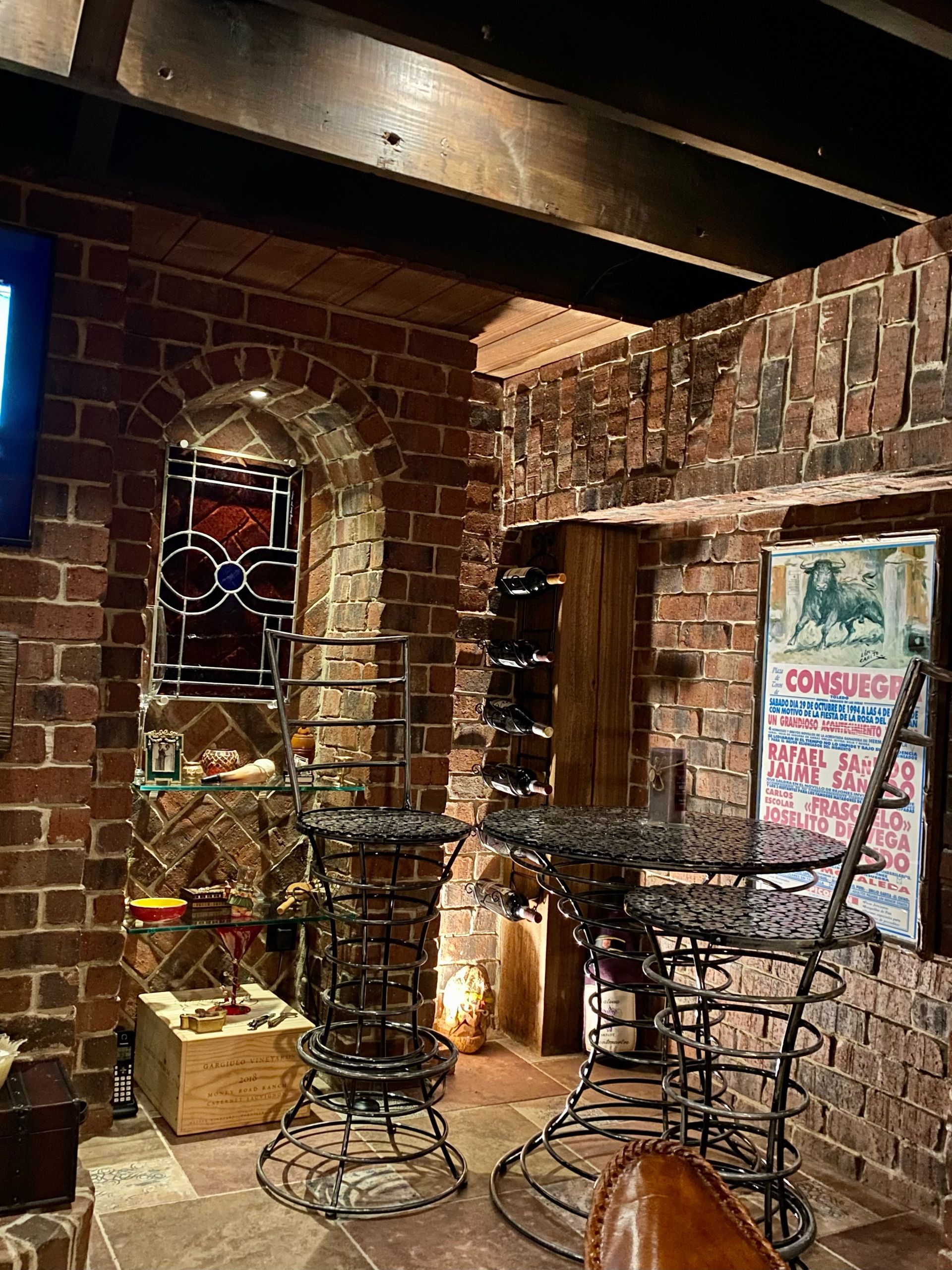 Brick-walled room with metal bar stools, stained glass window, and a vintage poster.