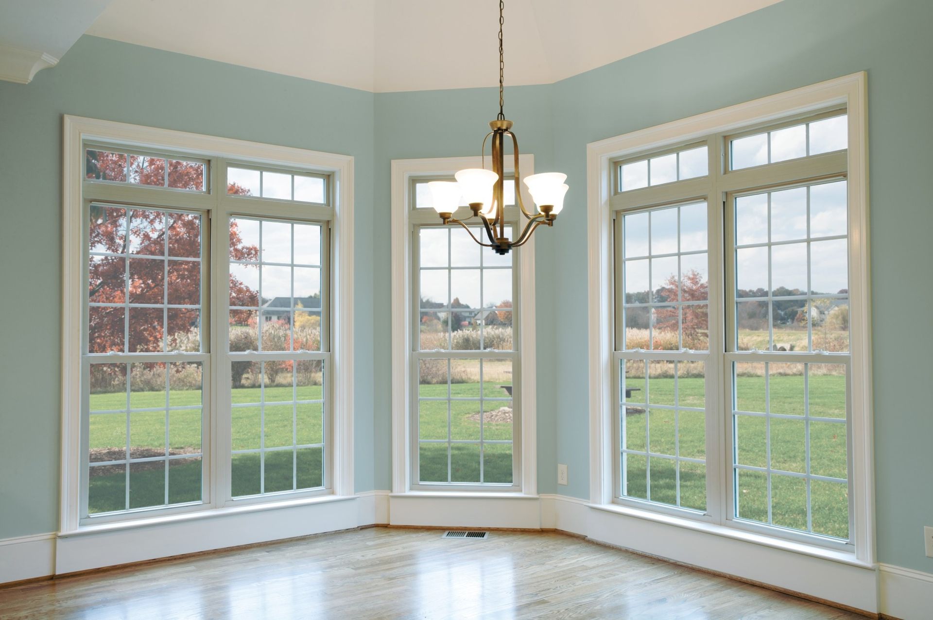 Corner room with three tall windows, blue walls, and a chandelier, overlooking a green lawn.