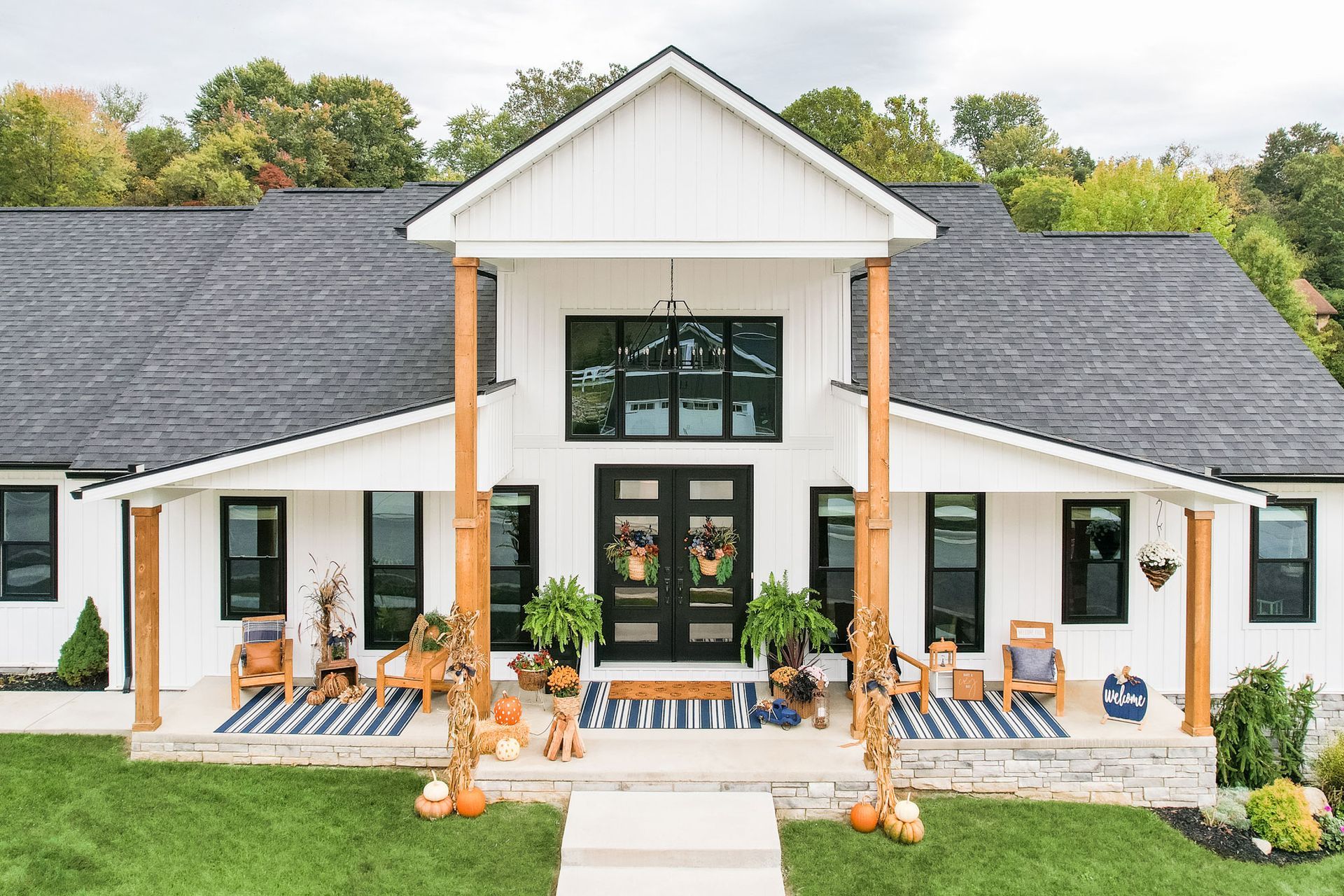 White farmhouse with black trim, fall decor, pumpkins on porch.