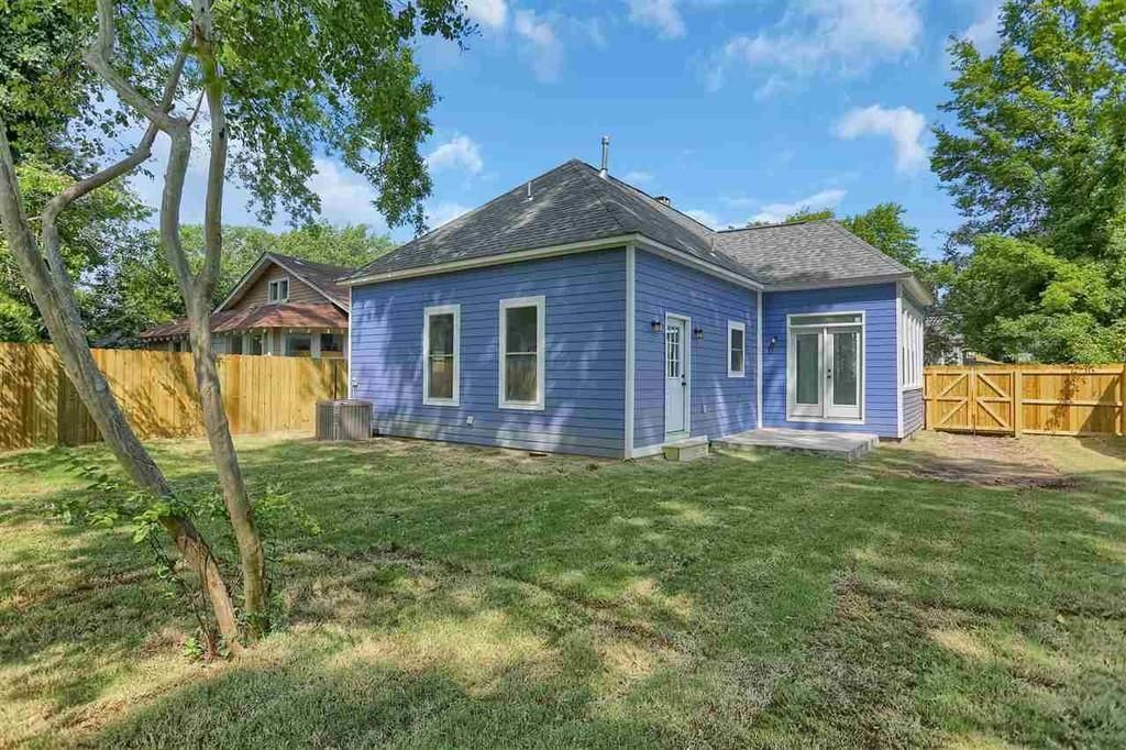 Blue house with white trim, set in a grassy yard, with a wooden fence and trees.