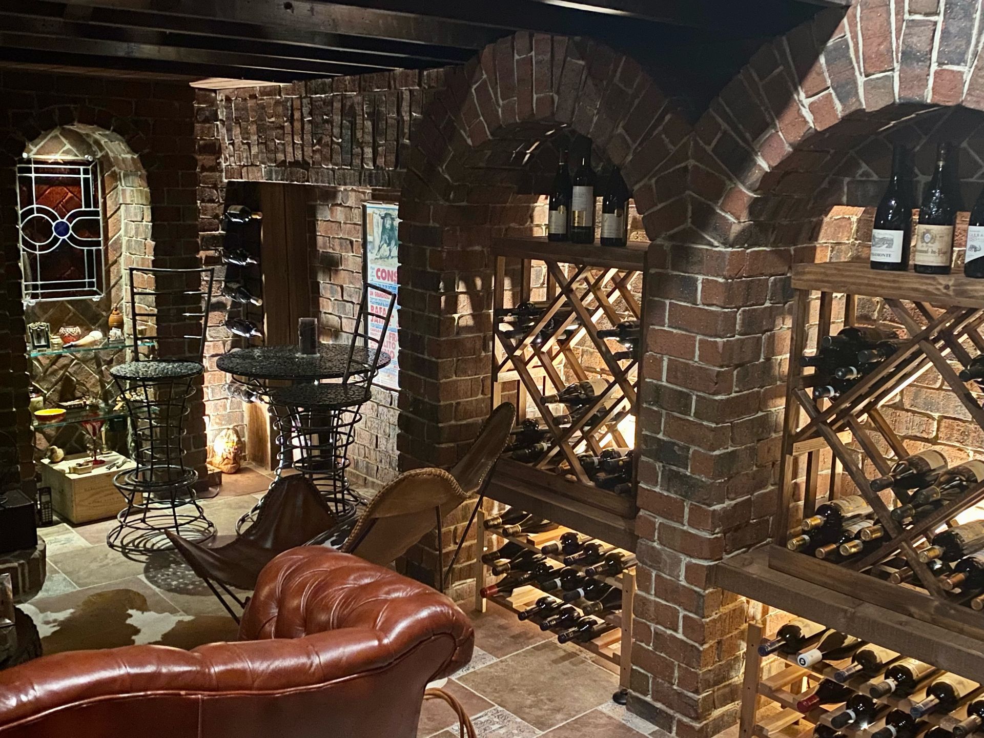 Wine cellar with brick arches, built-in wooden wine racks, and seating area with a leather sofa.