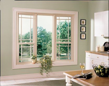 Cream-colored window in a light green room with a view of trees, a counter, and a table with a glass.