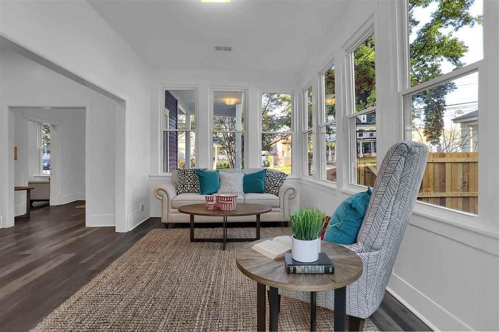 Bright sunroom with a couch, chair, and coffee table; wooden floors, windows.