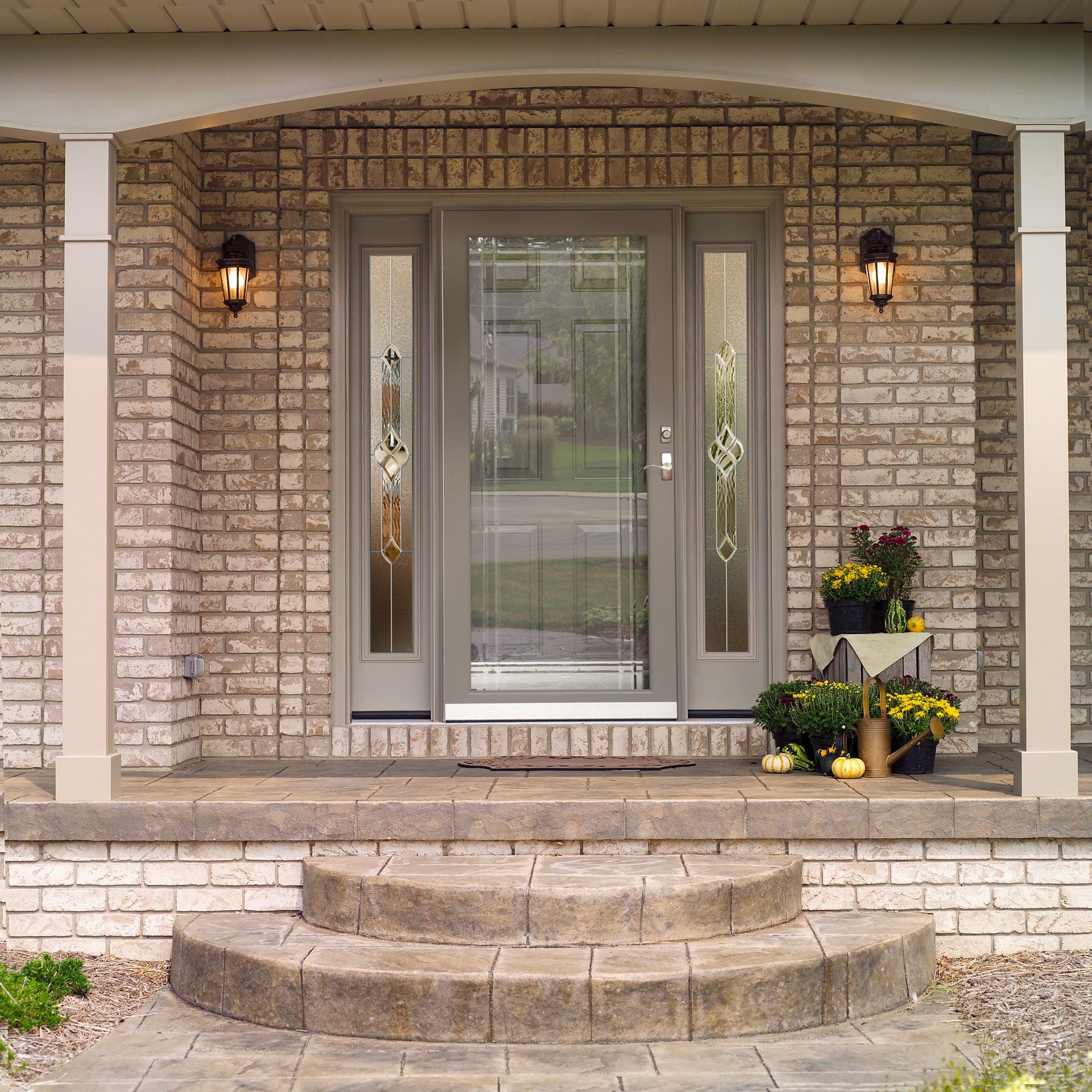 Brick home entrance with steps, door, sidelights, porch, and columns.