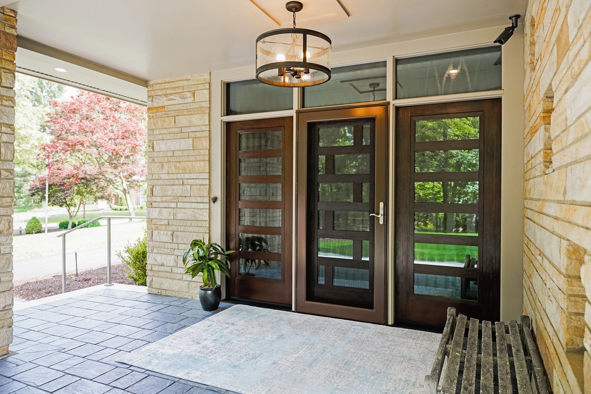 A covered entryway with stone walls, brown doors with glass panes, and a rug.