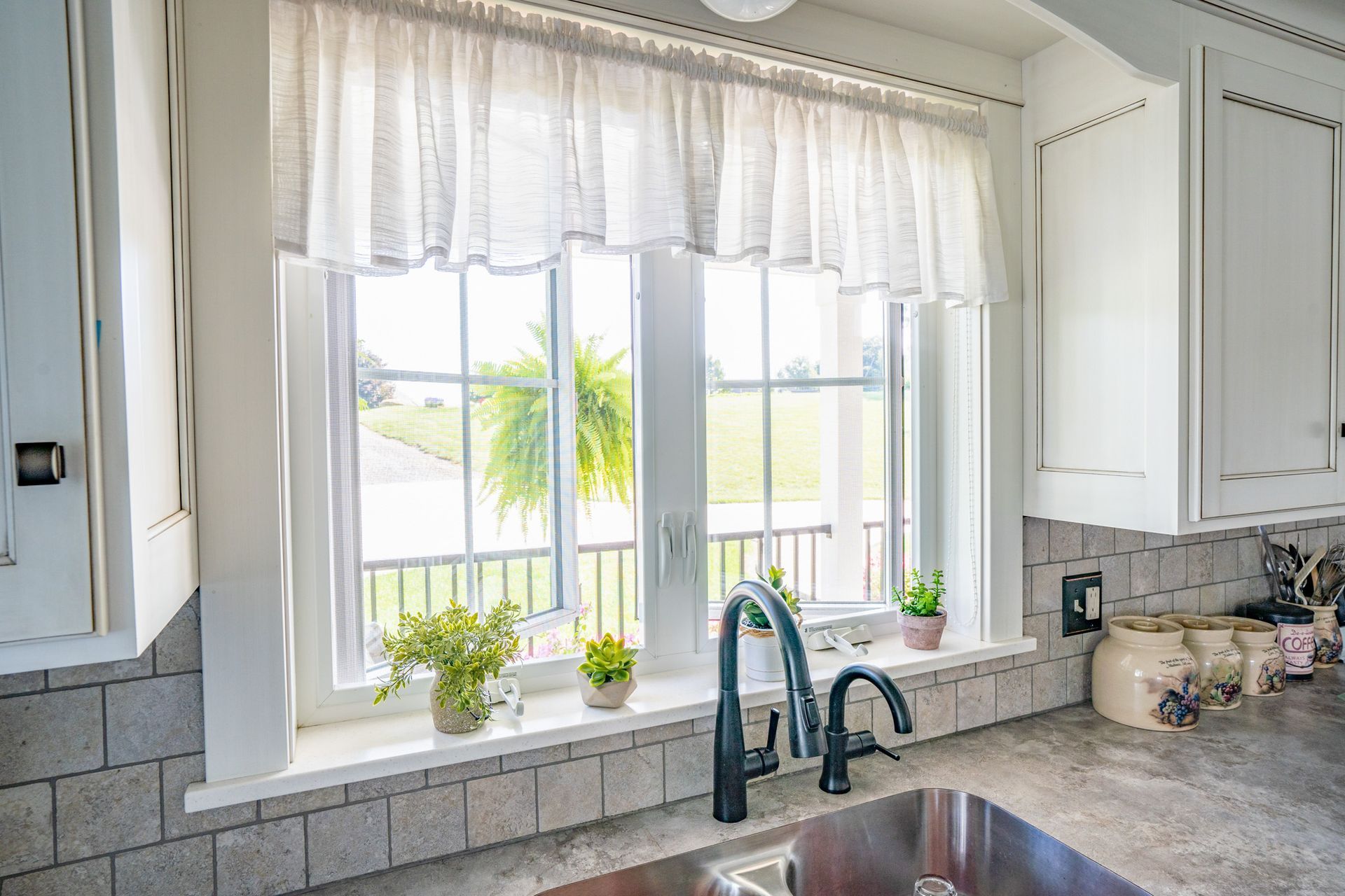 Kitchen sink with a window, white cabinets, and a decorative white curtain.
